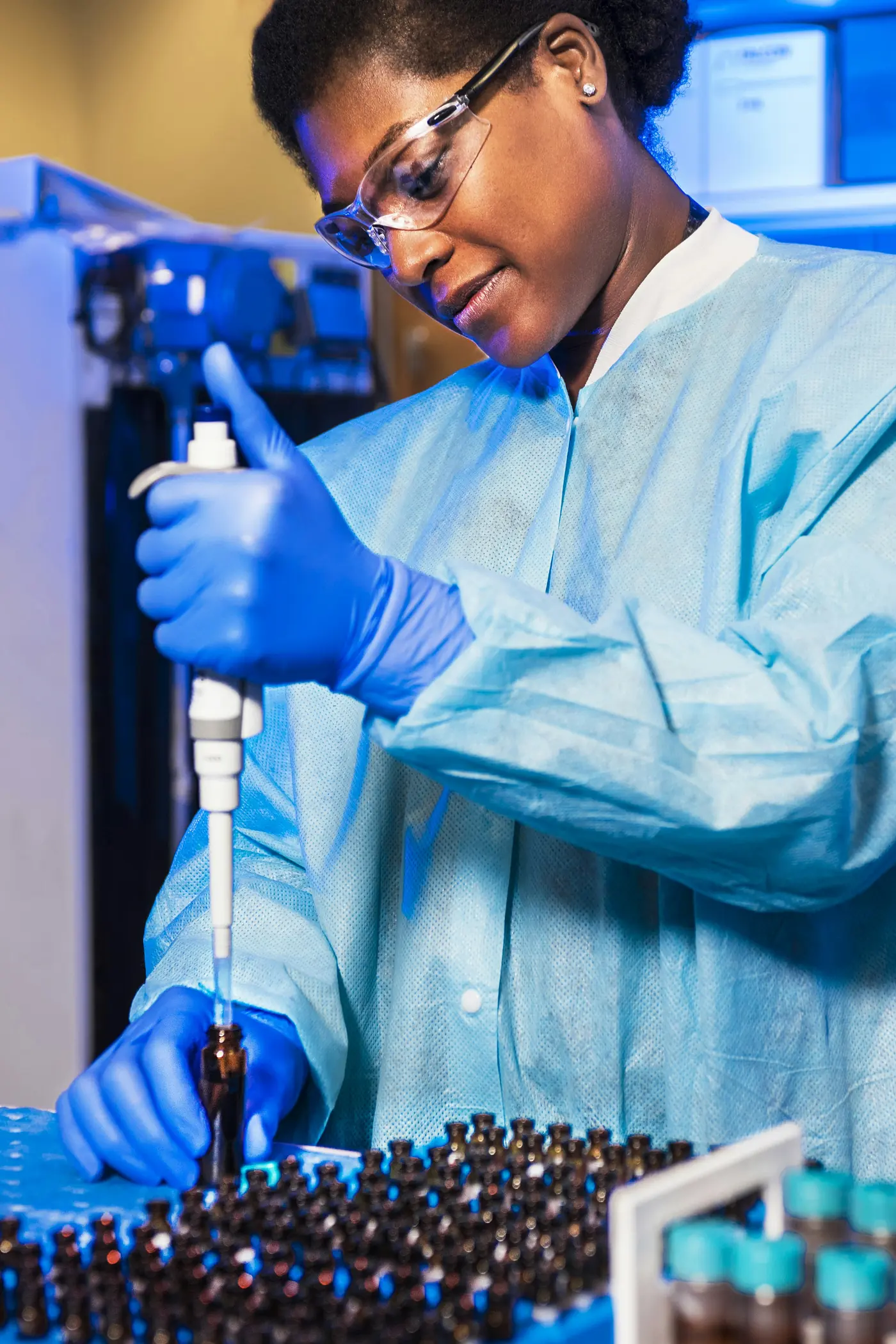 Un científico con bata azul y guantes usando una pipeta en un laboratorio